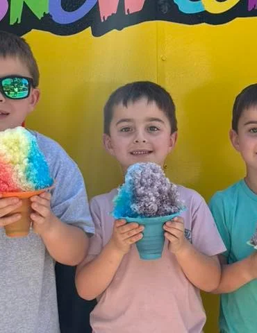 Children holding colorful snow cones in front of the Make It SnowCone truck